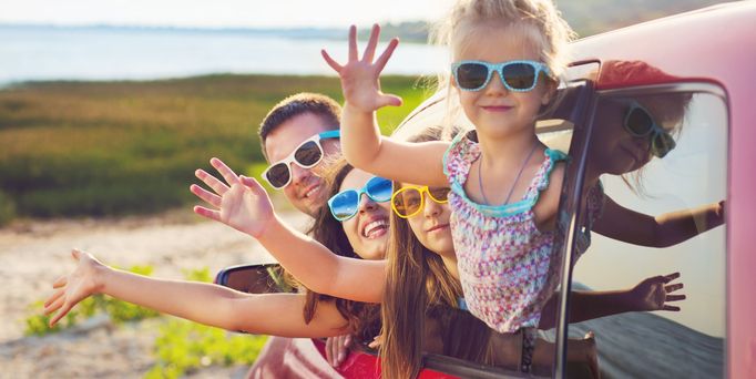 Familie schaut aus einem Autofenster und winkt 
