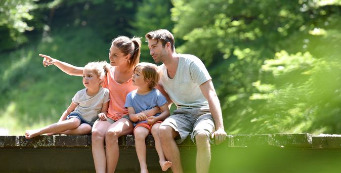 Deals. Eigenanreise. Familie sitzt auf einer Brücke im Wald 