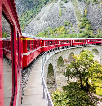 Roter Zug fährt über eine Brücke in den Bergen 