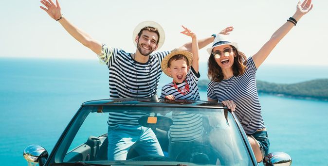 Familienurlaub. Familie sitzt mit ausgebreiteten Armen im Cabrio 