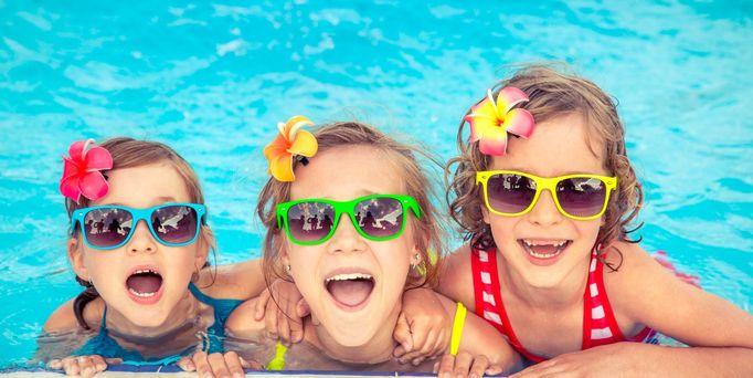 Familienurlaub. Drei Mädchen mit Sonnenbrillen  haben Spaß im Pool und lächeln in die Kamera 