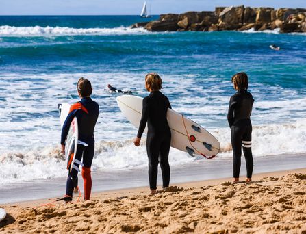 Portugal. Drei Surfer am welligen Meer 